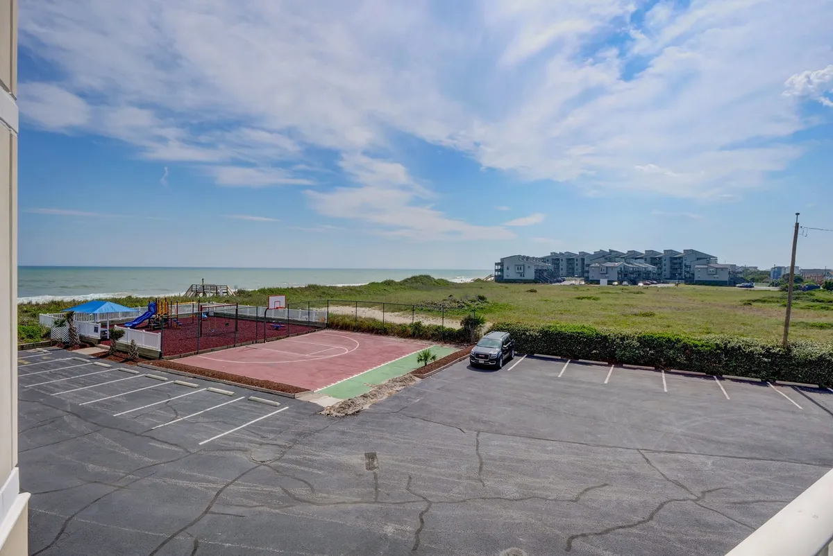 A panoramic view of the resort’s exterior captures the lively basketball court, a colorful playground bustling with children, the sandy beach in the background, and the sparkling ocean beyond. The scene showcases multiple family activity zones in one view.