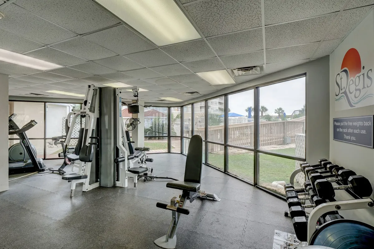 A modern fitness center featuring a variety of exercise equipment, large windows that let in plenty of natural light, and clear fitness center signage. The vibe is energetic, and the equipment supports both cardio and strength training activities.