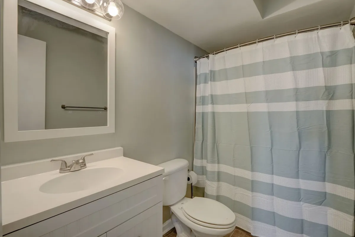 A bright and functional bathroom with a modern vanity, a large mirror, and a shower curtain. The space looks clean and thoughtfully appointed, designed for refreshing mornings or winding down after a day at the beach.