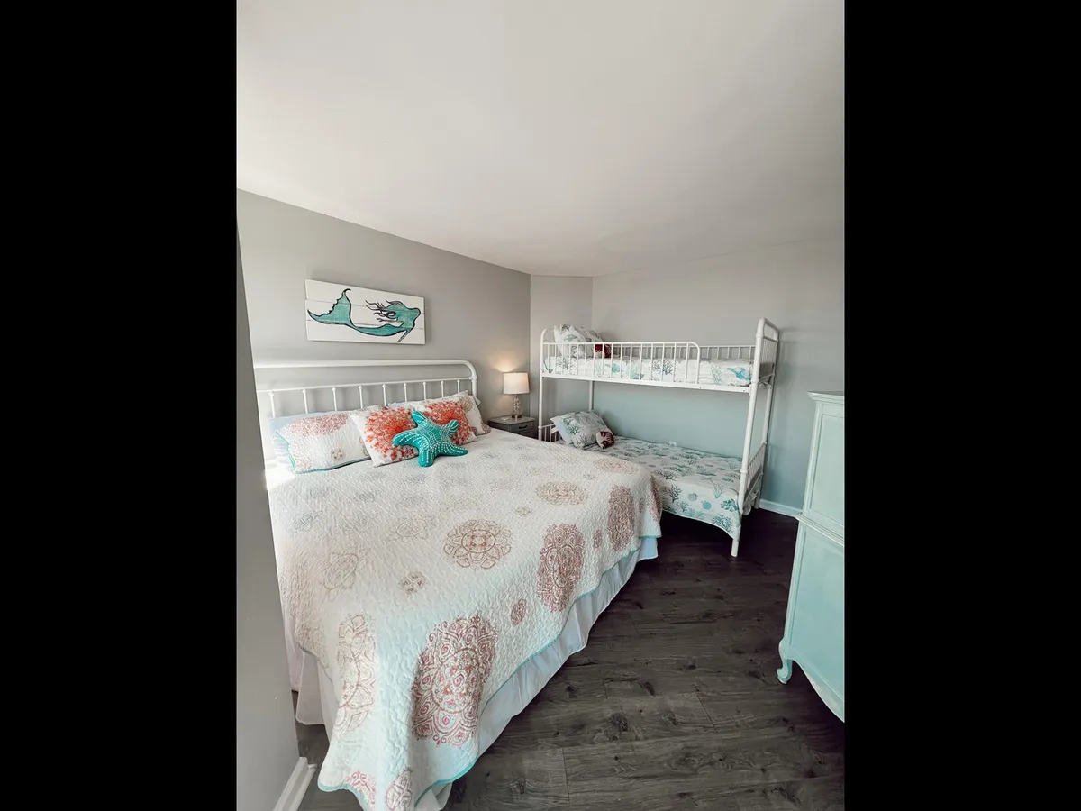 A cheerful bedroom with a large bed covered in a quilt, a bunk bed for extra sleeping space, playful starfish and wall art décor, and plenty of natural light. The setup is inviting, making it perfect for families or groups.