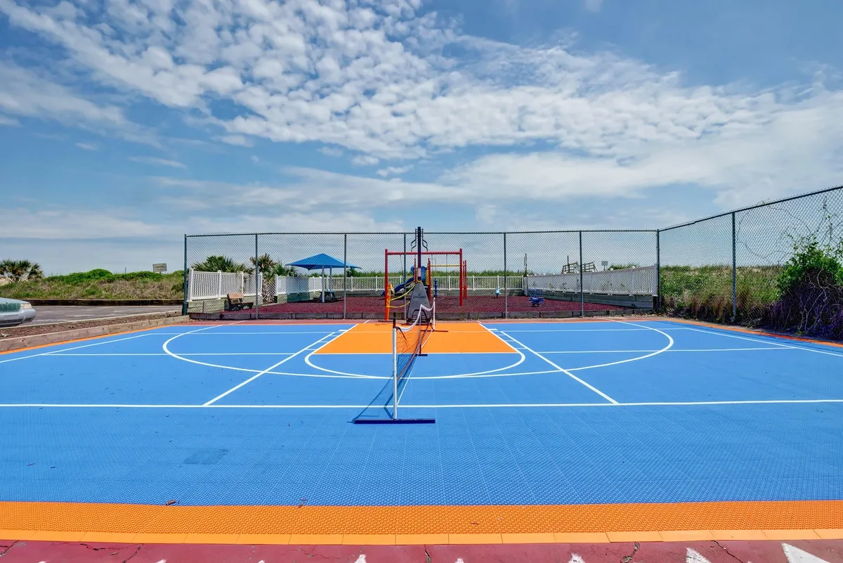 A colorful, versatile outdoor court equipped for basketball and tennis, featuring a hoop, net, and vibrant surface. The open sky and inviting layout suggest opportunities for fun and friendly competition.